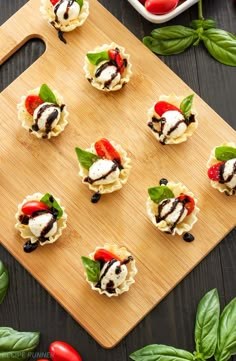 small appetizers on a wooden cutting board with basil leaves and tomatoes in the background