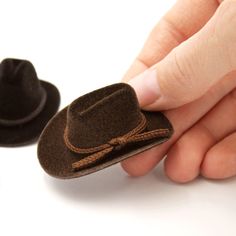 a hand holding a brown hat next to a black hat