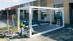 two men working on a metal structure in front of a building with windows and doors