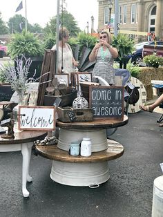 two women standing in front of a table with some items on it and one holding a sign that says come in awesome