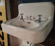 a white sink with two faucets on the wall next to a yellow sign