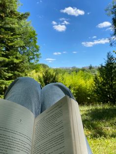 an open book sitting on top of a grass covered field under a blue cloudy sky