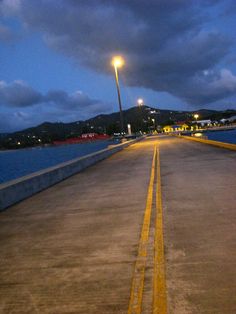 an empty parking lot next to the ocean at night with street lights on and dark clouds in the sky