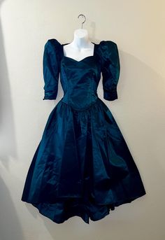 This vintage 80s party/prom dress is a stunning piece that will make you stand out at any party or special occasion. The dress is made of high-quality dark green satin stiff material. This dress is perfect for wearing as is to a retro 1980s gala or would be a great start to a gothic black Halloween costume. This has a sweetheart neckline. The bodice is fitted and has 3/4 ruched sleeves that are puffed at the shoulders bottom of sleeve is fitted, zips at back waist with a peekaboo Center, bow at the back of the shoulders. and has a super full midi Hilo skirt. No size tag, I believe it should fit a modern small size, (please note this has been altered and I believe you could get another inch if taken out at the bustline & waist) but please refer to the actual measurements below for a proper Black Halloween Costume, 1980s Prom Dress, Prom Dress Green, 1980s Prom, Black Halloween Costumes, Wedding Costume, 80s Party, Wedding Costumes, Green Prom Dress