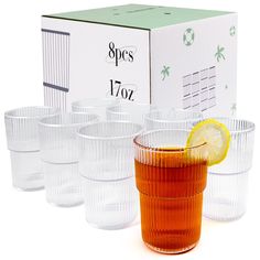 a set of six glasses with a lemon slice on the rim and an empty box behind them