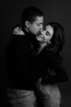 a man and woman embracing each other while posing for a black and white photo in front of a dark background