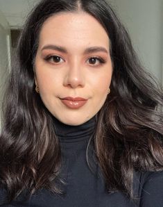 a woman with long dark hair wearing a black turtle neck top and gold hoop earrings