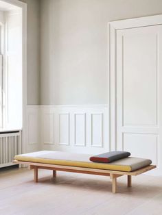 a bed with two pillows on top of it in front of a white wall and wooden floor