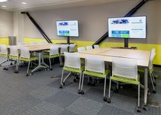 an empty conference room with tables and chairs in front of flat screen tvs on the wall