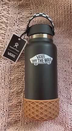 a black and brown water bottle sitting on top of a pink blanket next to a tag that says vans off the wall