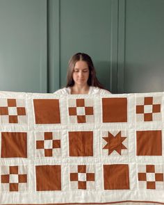 a woman is holding up a quilt made with squares and stars in brown and white