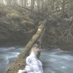 a woman laying on a log in the middle of a river with water rushing behind her