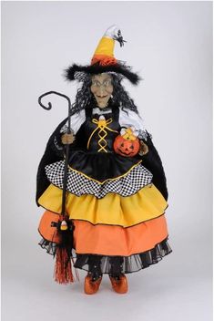 a doll dressed up as a witch holding a broom and pumpkin on a white background