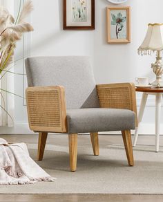 a beige chair sitting in front of a white wall next to a table with a lamp on it