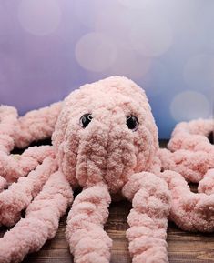 a pink octopus stuffed animal laying on top of a wooden table next to a purple wall