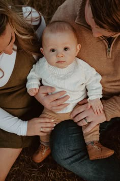 a man and woman holding a baby in their arms while sitting on the ground with hay