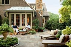 two people sitting on chairs in front of a house with potted plants and trees