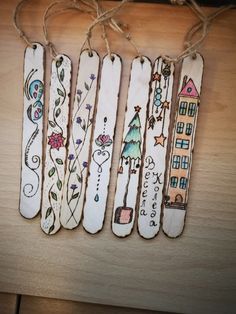 four wooden bookmarks with designs on them hanging from twine strings in front of a wood table