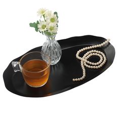 a cup of tea and some pearls on a tray with flowers in a glass vase