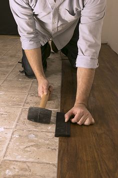 a man laying tile on the floor with a hammer