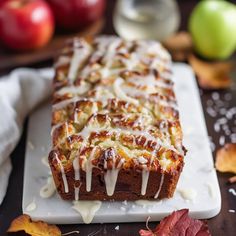 a loaf of cinnamon apple bread with icing on a cutting board next to apples