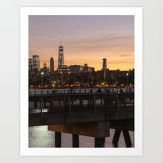 the city skyline is lit up at night as seen from across the water in front of a bridge