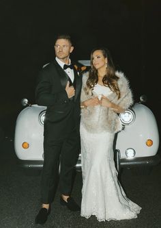 a man and woman standing next to each other in front of a car