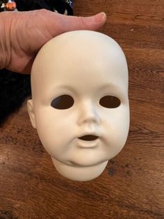 a person holding up a white mask on top of a wooden table