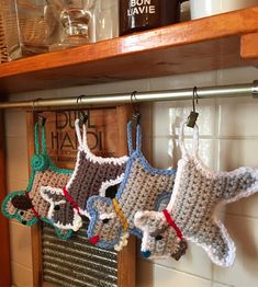 three crocheted animals hanging from hooks on a kitchen shelf next to a mug