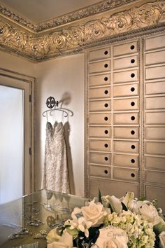 a wedding dress hanging on a hanger next to a bouquet of flowers and wine glasses