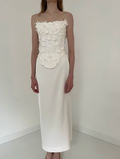 a woman standing in front of a white wall wearing a dress with flowers on it