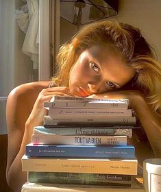 a woman leaning her head on top of a stack of books