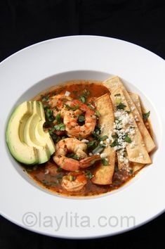 a white plate topped with tortilla and shrimp next to an avocado