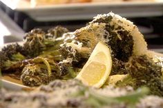 some broccoli and lemon slices on a plate with other food in the background