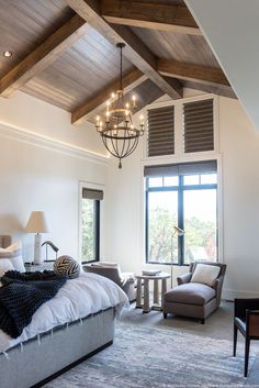 a bedroom with a bed, chair and chandelier in front of a large window