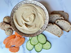 a bowl of hummus next to sliced carrots and cucumbers