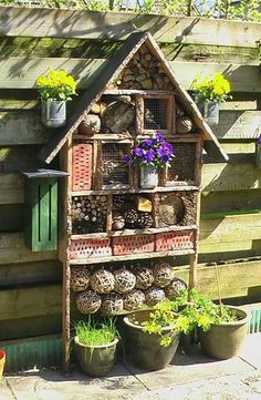 a bird house made out of wood with plants and flowers in pots next to it