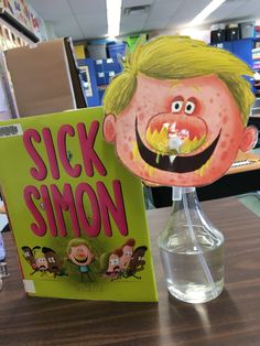 there is a book about sick smon on the table next to a vase with water in it