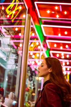 a woman standing in front of a store window looking at the lights on the building