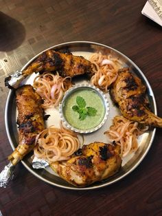 a plate with chicken wings and noodles on it, garnished with green sauce