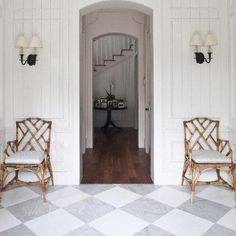 two chairs sitting in front of an open door on a checkered floor with chandelier above them