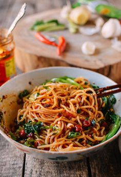 a bowl filled with noodles and vegetables on top of a wooden table next to some chopsticks