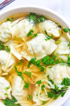 a white bowl filled with dumplings covered in broth and green garnish