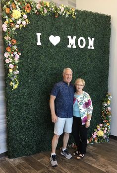 a man and woman standing in front of a wall with the words i love mom written on it