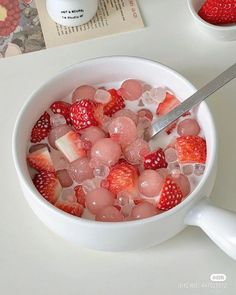 a bowl filled with ice and strawberries on top of a white table next to a book