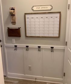 a calendar hangs on the wall next to two hooks and a toilet paper dispenser