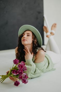 a woman laying on the floor next to a bouquet of flowers and wearing a green hat