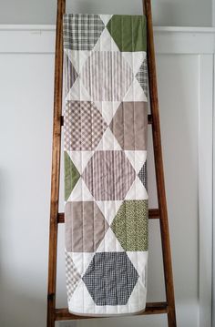 a wooden ladder holding a quilt on top of a white wall next to a window