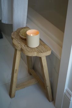 a candle sitting on top of a wooden stool next to a bath tub