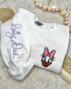 Cozy up in a bit of magic with our enchanting, Magical Autograph crewneck sweater. This sweater has a soft blended interior and features an embroidered face of the beloved Mrs. Duck on the left side of the chest and her autograph alongside the right sleeve. It could not get any cuter than this! ✦Sweater design features two embroidered locations. ✦Choose your preferred colored crew! ✦Interested in a different character? Head over to our "All Crewnecks" tab or type 'Magical Autograph Crewneck' in the search bar to see the other characters! ✦Want to pair this sweater with our mouse ears? Browse our ear selection to find your favorite match! White Crew Neck Sweater With Letter Embroidery, Cute Crew Neck Embroidered Sweatshirt, Cute White Embroidered Sweatshirt, White Embroidered Sweatshirt For Winter, Cute Letter Embroidery Sweatshirt For Winter, White Letter Embroidery Sweater For Winter, Cute White Sweater With Embroidered Text, White Cute Sweater With Embroidered Text, Cozy Embroidered Long Sleeve Sweatshirt